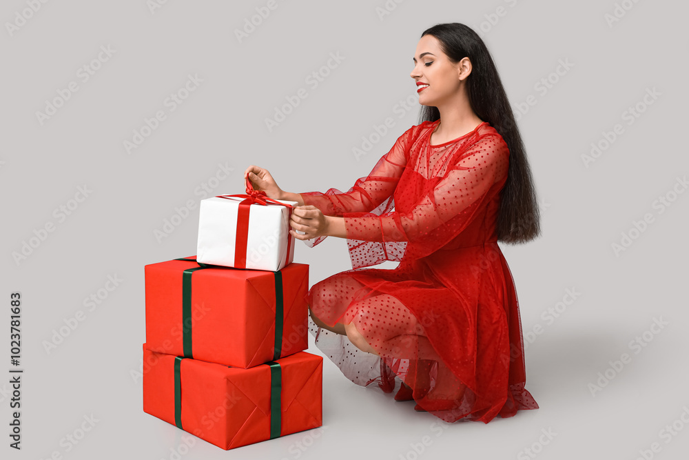 Beautiful young woman with Christmas gifts on grey background Beautiful young woman with Christmas gifts on grey background