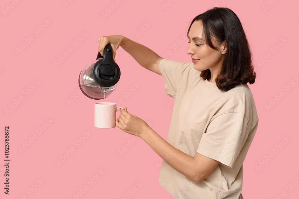Beautiful young woman pouring hot water from modern electric kettle into cup on pink background Beautiful young woman pouring hot water from modern electric kettle into cup on pink background