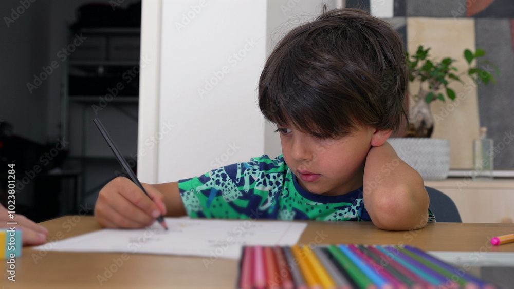 Young boy concentrating on his drawing, leaning on his arm, surrounded by colorful pencils and art supplies, engaged in a creative task at home Young boy concentrating on his drawing, leaning on his arm, surrounded by colorful pencils and art supplies, engaged in a creative task at home