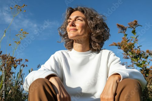 Happy mature woman wearing white blank sweatshirt and brown pants, relaxing in nature on wonderful sunny autumn day