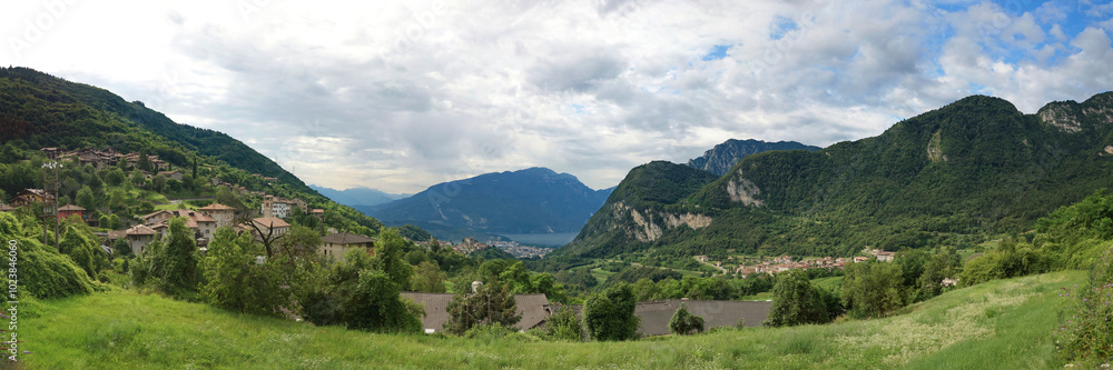 Naklejka premium Panorama Aussicht ins Tal mit mehreren mediteranen Italienischen Bergdörfern, Wald und einem See im Sommer bei bewölktem Himmel.