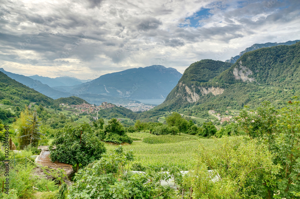 Naklejka premium Aussichtspunkt ins Tal mit mehreren mediteranen Italienischen Bergdörfern, bewachsenen Feldern, Wald und einem See im Sommer bei bewölktem Himmel.