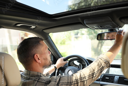 Man adjusting rear view mirror while driving car