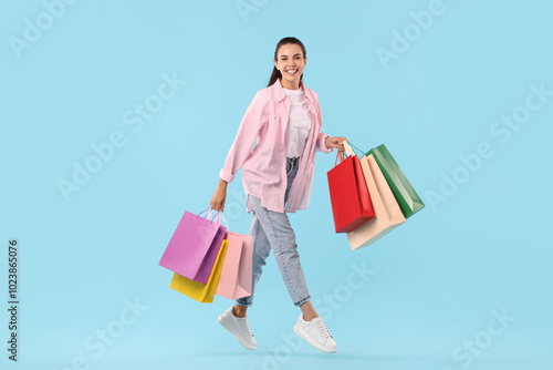 Smiling woman with colorful shopping bags jumping on light blue background