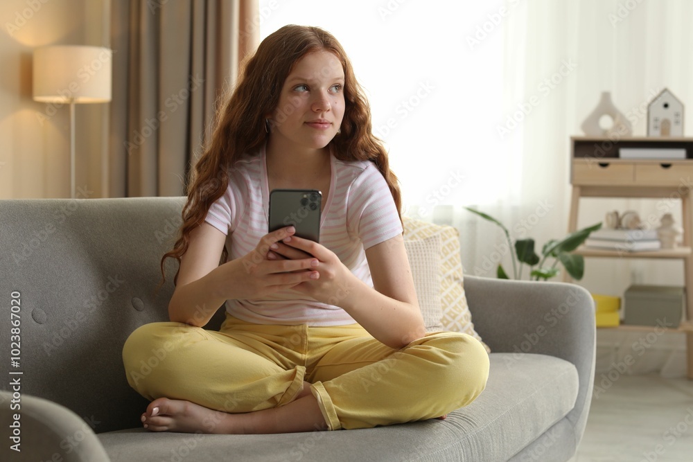 Fototapeta premium Beautiful teenage girl using smartphone on sofa at home