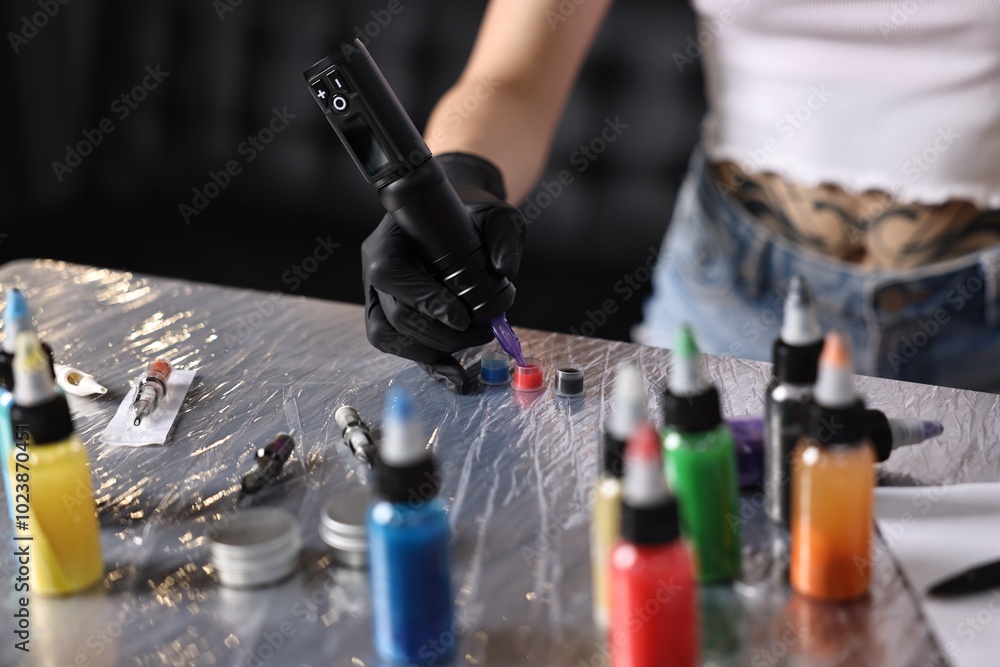 Fototapeta premium Professional artist working with tattoo machine and inks at sterile table in salon, closeup