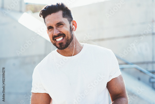 portrait of cheerful man dressed in blank t shirt enjoying free time for listening music songs via electronic headphones,happy male with modern smartphone device smiling at camera photo