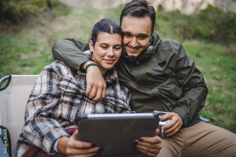 happy couple campers sit and watch movie on tablet in front tent happy couple campers sit and watch movie on tablet in front tent