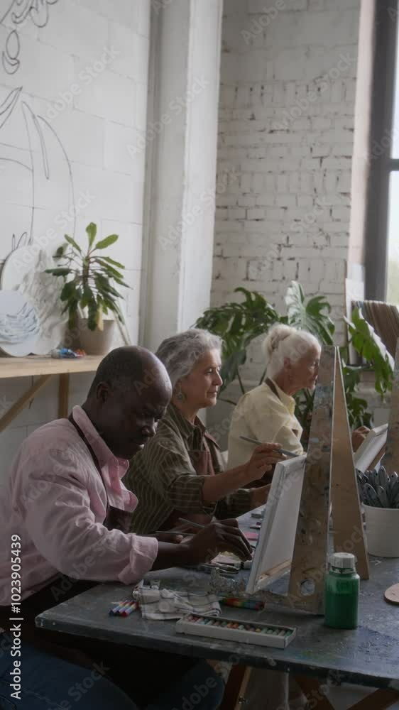 Vertical view of group of diverse senior people in aprons painting on canvases during art workshop in studio Vertical view of group of diverse senior people in aprons painting on canvases during art workshop in studio