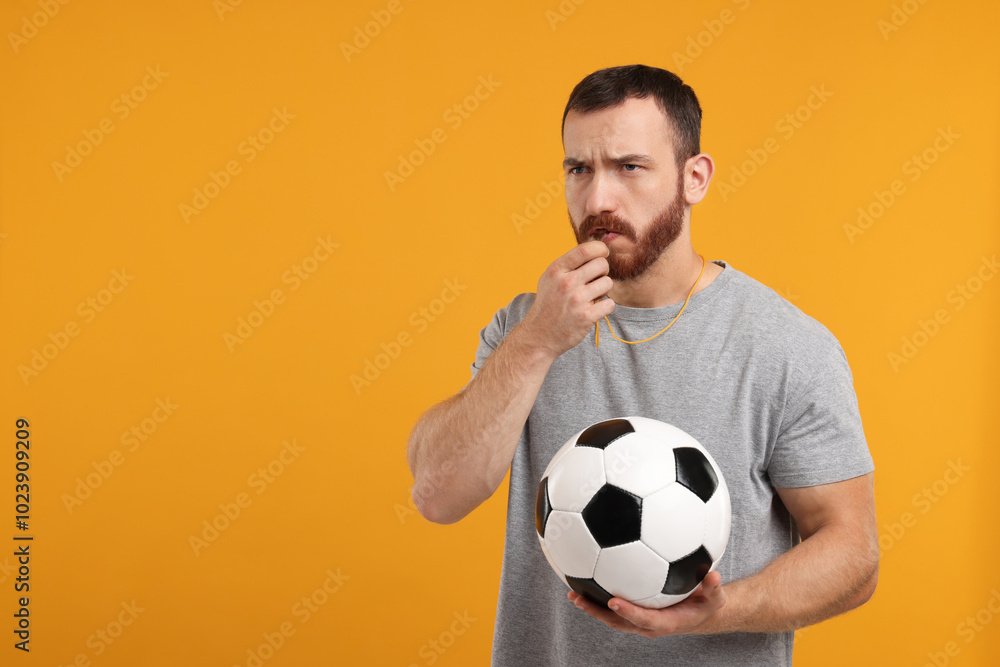 Young man with soccer ball blowing whistle on orange background, space for text Young man with soccer ball blowing whistle on orange background, space for text