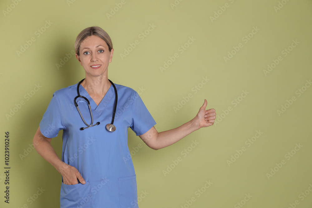 Nurse in medical uniform with stethoscope showing thumbs up on light green background Nurse in medical uniform with stethoscope showing thumbs up on light green background