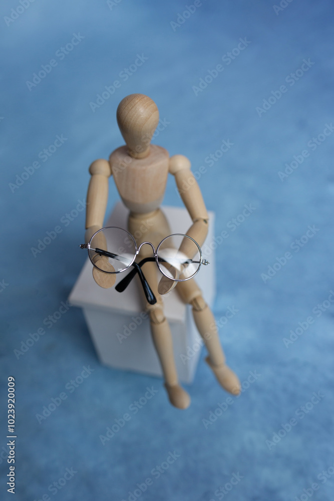 Wooden mannequin sitting on a stool with glasses in hands. Vision problems concept. Computer work ophthalmology Wooden mannequin sitting on a stool with glasses in hands. Vision problems concept. Computer work ophthalmology