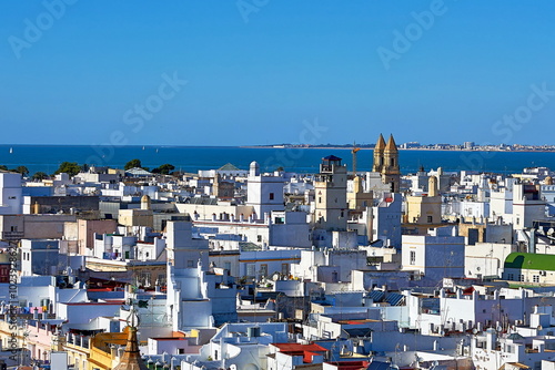 Rooftop view of Cádiz with whitewashed buildings, historic towers, and a distant coastline, set against a backdrop of blue skies and calm waters photo