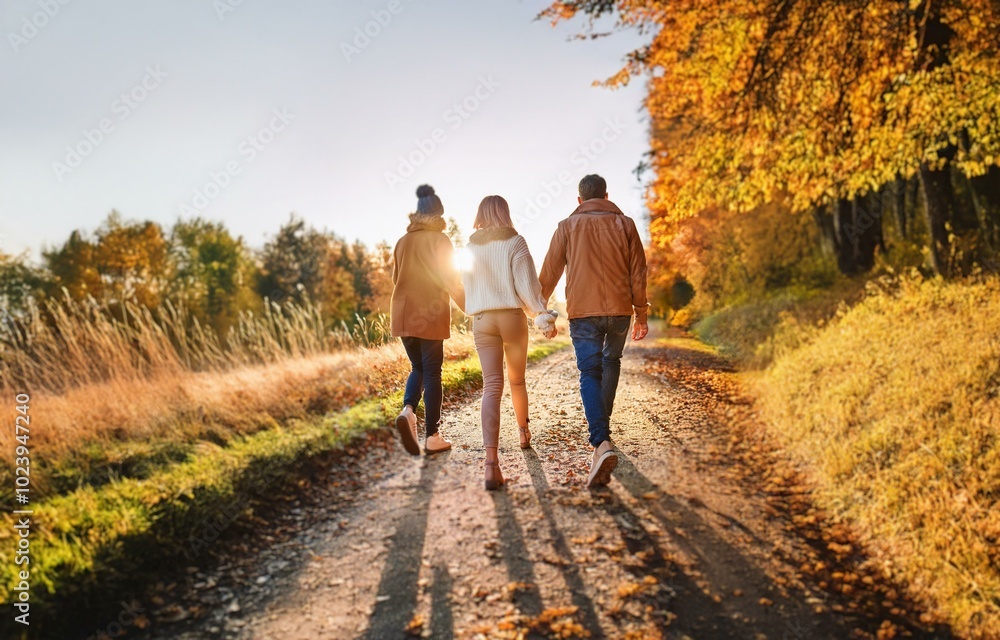 Three people walk along a path in a forest during the autumn season. Three people walk along a path in a forest during the autumn season.