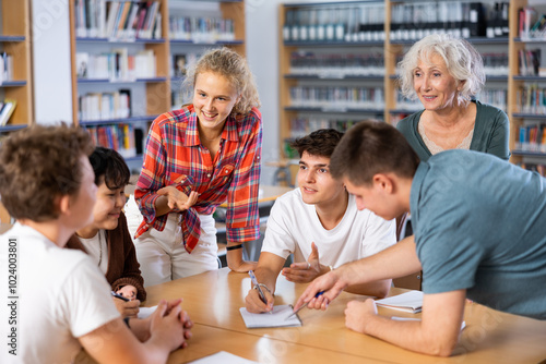 Teenage girl tells an interesting story to his friends in the school library photo