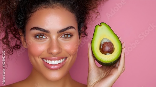 Young smiling woman holding half of an avocado representing a natural vitamin enriched facial treatment against a vibrant pink wall with a complementary color scheme The image showcases a fresh