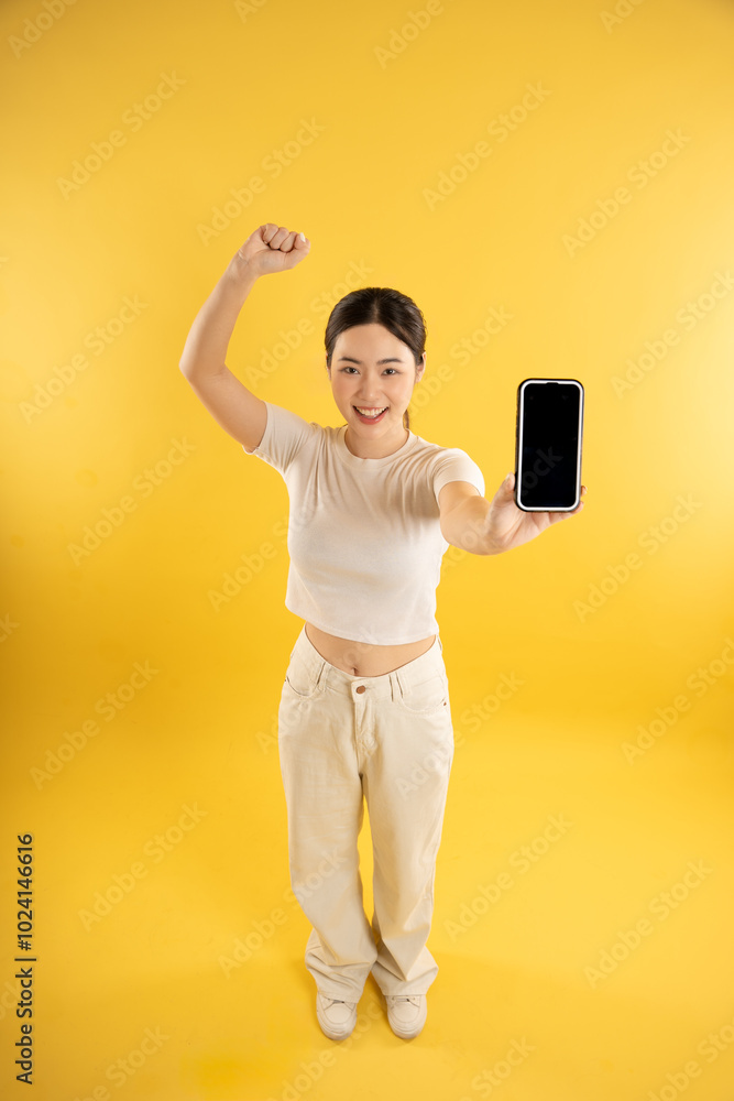 Full body image of young Asian girl using phone and posing on yellow background Full body image of young Asian girl using phone and posing on yellow background