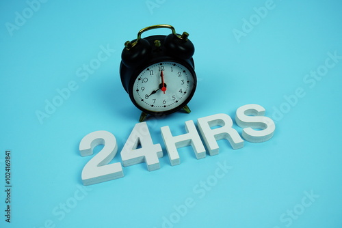 24 Hrs alphabet letters and alarm clock top view on blue background photo