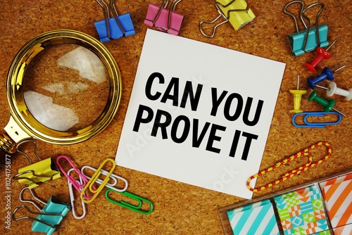 Can You Prove It text on paper card with magnifying glass and stationery on cork board background photo