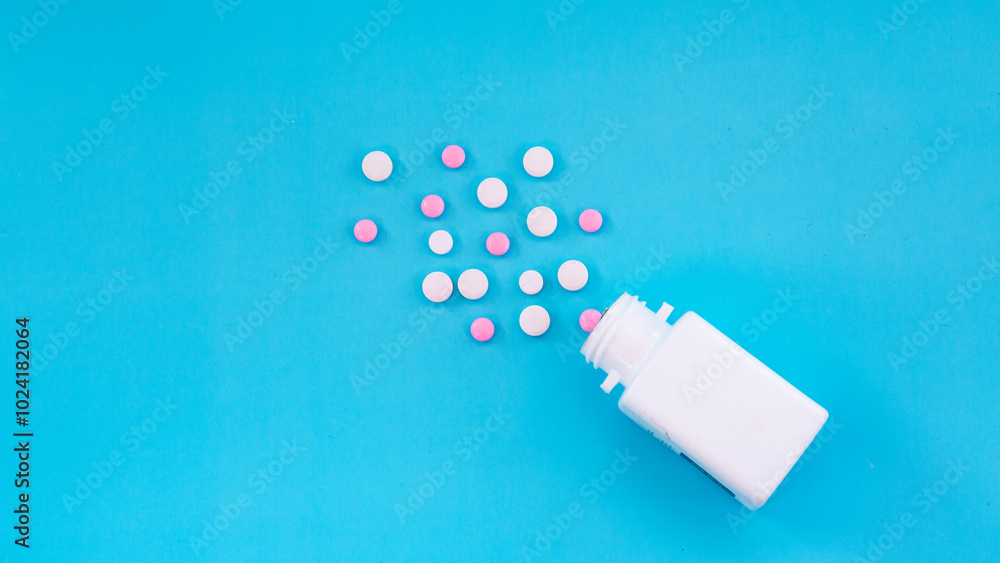 Flat lay of white bottle with white and pink medicine pills spread out on blue background. Concept of drugstore, pharmacy, healthcare, medicine, pharmaceutical business. Flat lay of white bottle with white and pink medicine pills spread out on blue background. Concept of drugstore, pharmacy, healthcare, medicine, pharmaceutical business.
