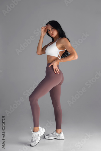 Portrait of sporty athletic woman in white sportswear doing stretching, enjoying sport exercises, stretching legs, practicing yoga. Shot indoors with big window