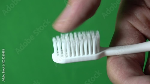 Close up shot male hand thumb touching to check softness of toothbrush bristles with green screen fabric in background.
