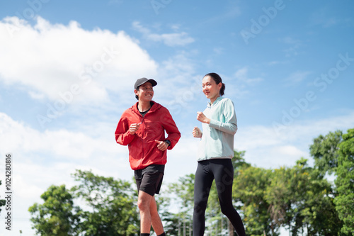 A young Asian couple wearing blue and red sportswear, the two of them jogging together. Ready to talk while running outdoor exercise Exercise in the stadium maintaining health exercise active living