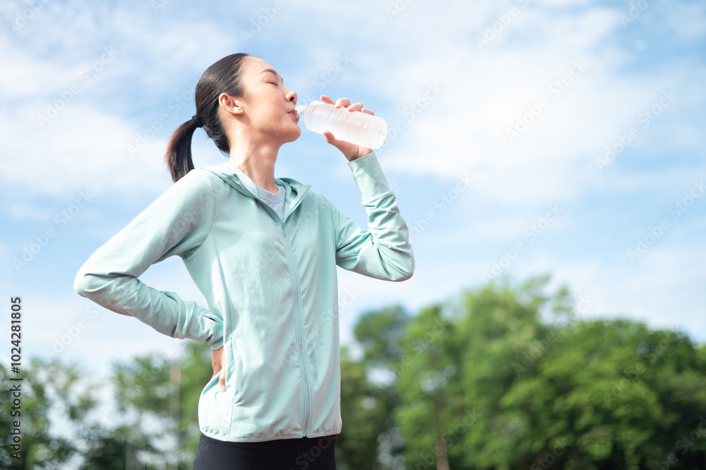 Asian woman wearing blue sportswear Stand and drink water after exercising. outdoor exercise Exercise in the stadium She is exercising and holding a water bottle. active living athletes drink water Asian woman wearing blue sportswear Stand and drink water after exercising. outdoor exercise Exercise in the stadium She is exercising and holding a water bottle. active living athletes drink water
