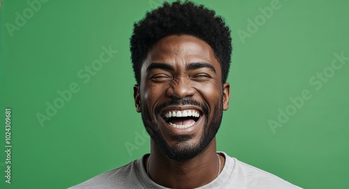 Young Black man with high brow laughing pale green background