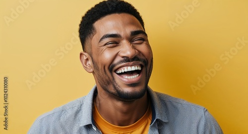 Young mixed race man with angular jawline laughing warm yellow background