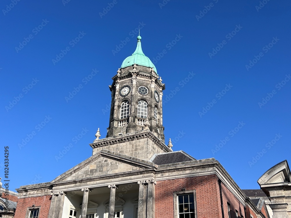 The clock tower of Dublin Castle stands tall with its distinctive green dome and clock face, set against a blue sky with scattered clouds