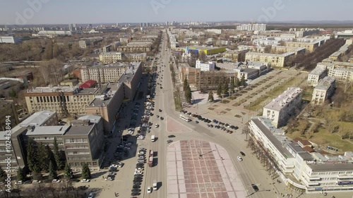 Aerial view of traffic in the city on a street with a roundabout and a square. Low-rise buildings

