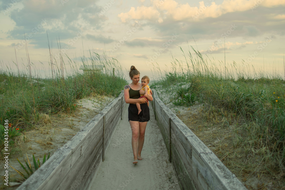 Mother and toddler walking on beach path at sunset Mother and toddler walking on beach path at sunset