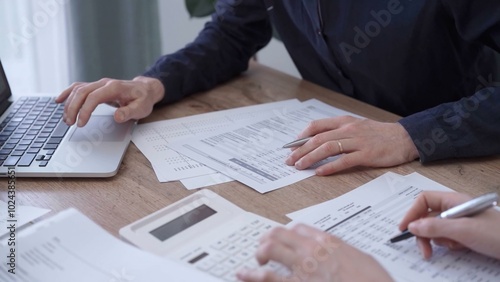 Close up of professional hands using a calculator to conduct financial analysis at the background of a colleague with a magnificent glass. Bookkeeping, finance audit and taxes