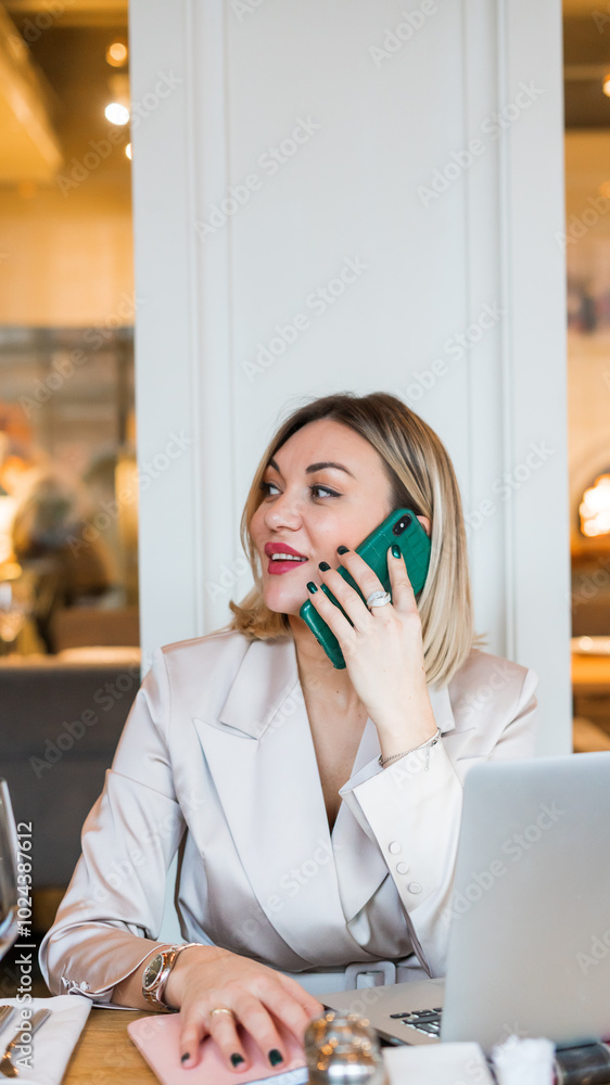A woman is sitting at a table with a laptop in a cafe. She is wearing a suit and working on her laptop. There are wine glasses, a bottle and a bowl on the table. Working atmosphere. A woman is sitting at a table with a laptop in a cafe. She is wearing a suit and working on her laptop. There are wine glasses, a bottle and a bowl on the table. Working atmosphere.
