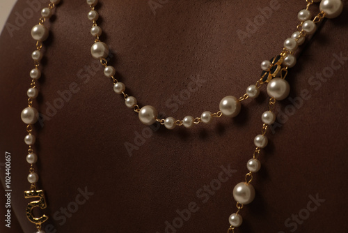 Close-up of dark-skinned young female model with pearl necklace on her shoulder posing over white wall.