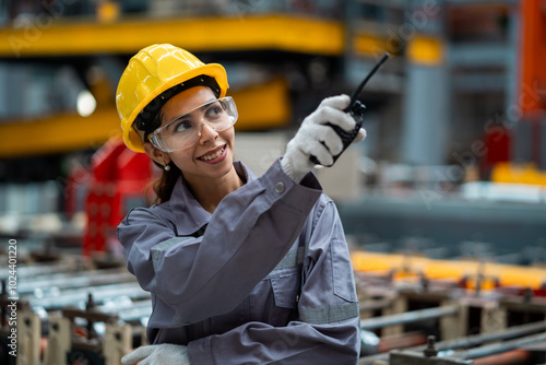 Tableau sur toile A woman wearing a yellow helmet and safety glasses is holding a walkie talkie