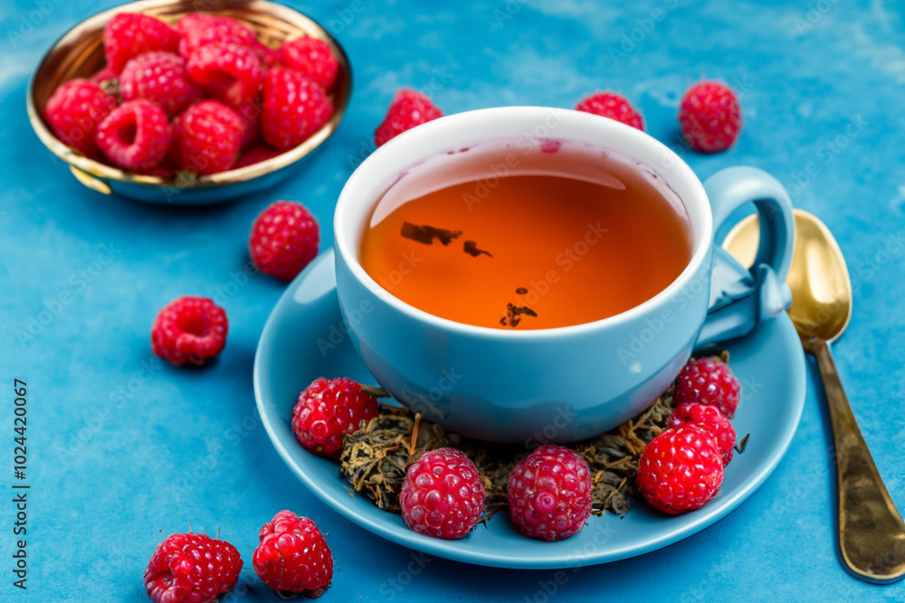 White with cup of tea and raspberry. food sweet fresh concept. mug with a cup of tea and raspberries on a blue . a mug with blue and red flowers and raspberries on it on lifestyle a. White with cup of tea and raspberry. food sweet fresh concept. mug with a cup of tea and raspberries on a blue . a mug with blue and red flowers and raspberries on it on lifestyle a.
