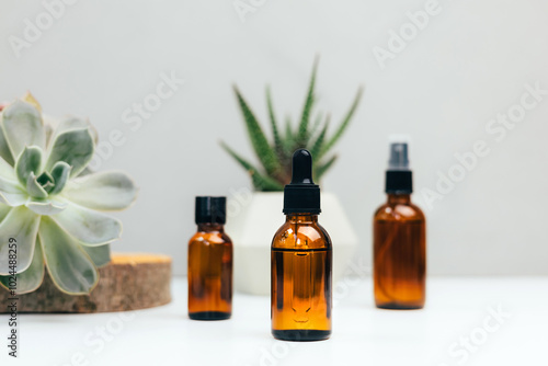 Natural cosmetics. Amber bottles with facial, bath liquid on a concrete background with a green succulent. Front view