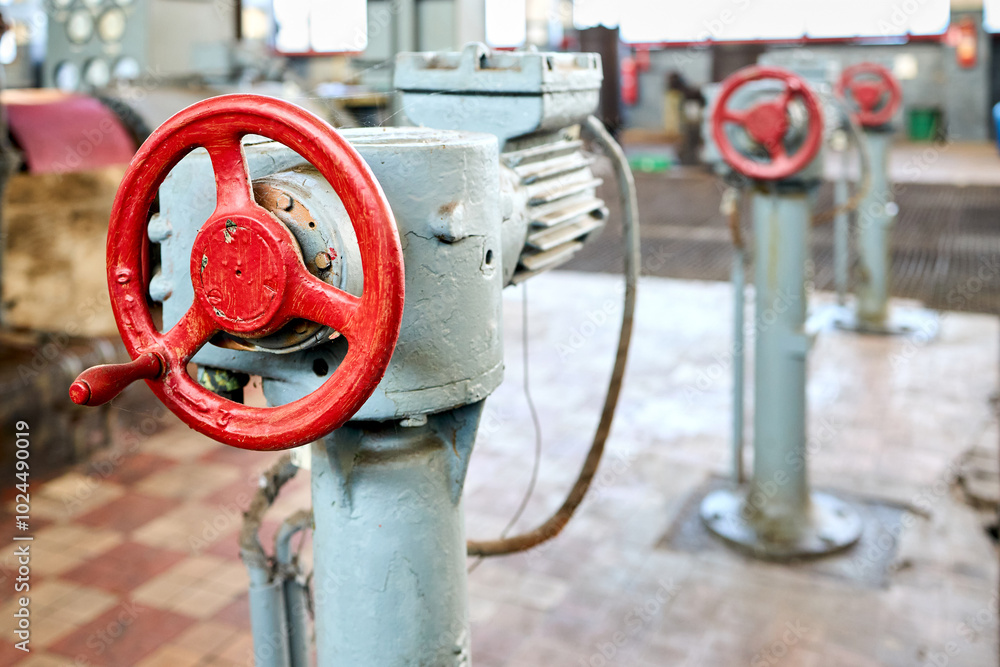 Row of old retro Motor drive electric valve wheels painted red selective focus with extension device over out of focus background tiled floor and perforated metal sheet stamping plates with copyspace. Row of old retro Motor drive electric valve wheels painted red selective focus with extension device over out of focus background tiled floor and perforated metal sheet stamping plates with copyspace.