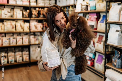 Beautiful young woman enjoying in modern pet shop together with her adorable brown toy poodle.