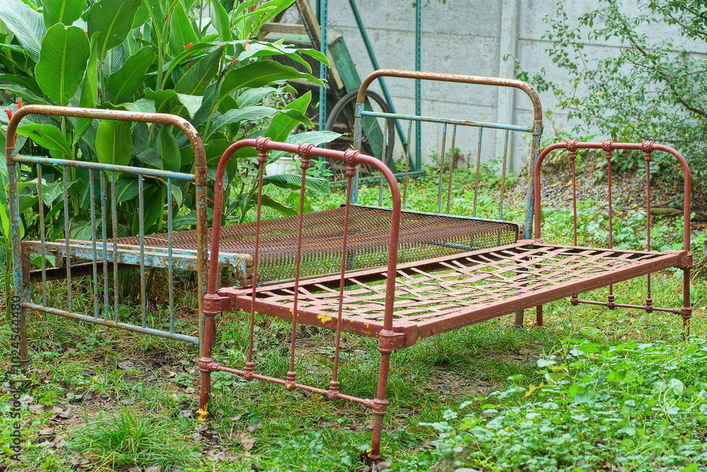 two different painted old iron heavy blue and brown industrial antique dirty rusty broken empty retro beds stand on the green grass near the leaves during the day on the street two different painted old iron heavy blue and brown industrial antique dirty rusty broken empty retro beds stand on the green grass near the leaves during the day on the street