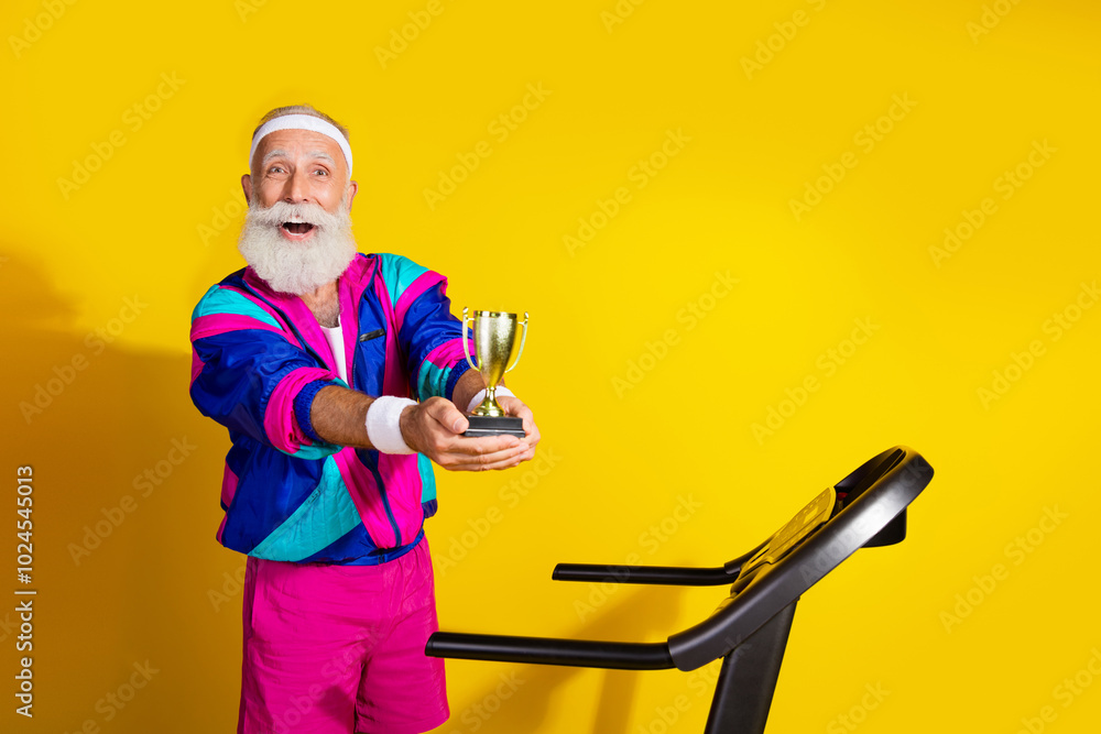 Photo portrait banner of funny senior sportsman hold golden goblet treadmill wear retro sport costume isolated on yellow color background Photo portrait banner of funny senior sportsman hold golden goblet treadmill wear retro sport costume isolated on yellow color background