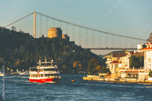 Ferry sailing on the Bosphorus under Fatih Sultan Mehmet Bridge in Istanbul, with Rumeli Fortress in background. Istanbul, Turkiye photo