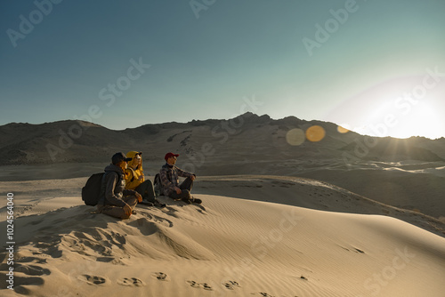 A group of people are sitting on the sand during the golden hour. Friends are sitting on the sand during sunset. A golden hour in the desert with people. Travelers are friends.