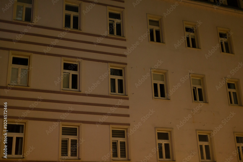 A tall and modern building featuring a large number of windows is beautifully lit up during the night, creating a mesmerizing view A tall and modern building featuring a large number of windows is beautifully lit up during the night, creating a mesmerizing view