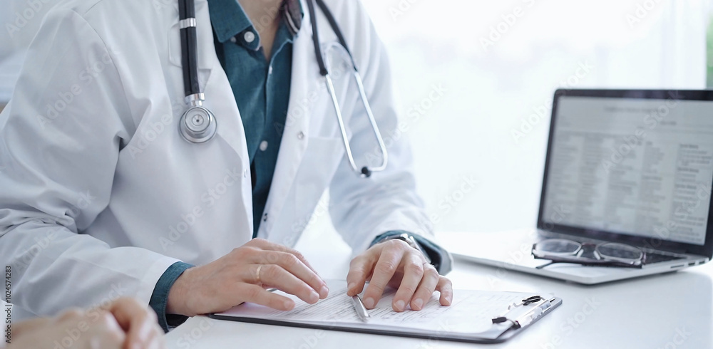 Doctor and a patient. The physician, wearing a white medical coat over a green shirt, is gesturing with his hands during a consultation in the clinic. Medicine Doctor and a patient. The physician, wearing a white medical coat over a green shirt, is gesturing with his hands during a consultation in the clinic. Medicine