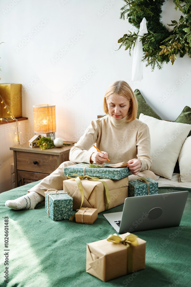 Mature woman write Christmas wishes on card. Packing gift and presents, season of giving. Christmas time. Mature woman write Christmas wishes on card. Packing gift and presents, season of giving. Christmas time.