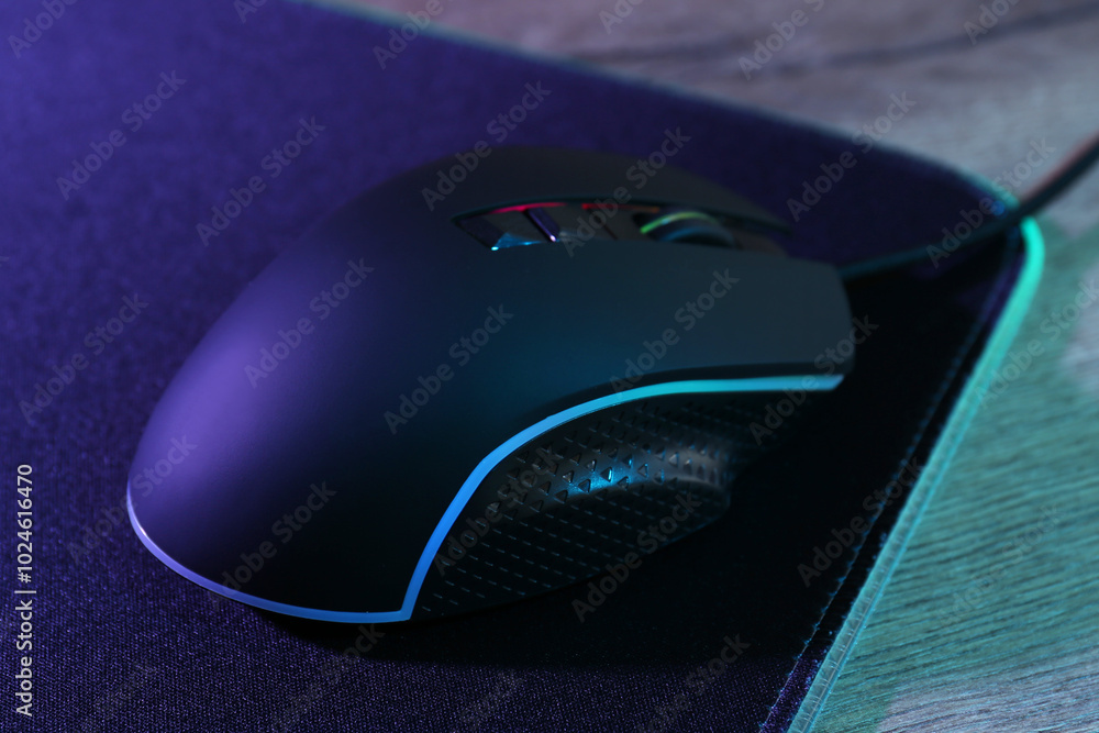Black computer mouse and mousepad on wooden table in neon lights, closeup Black computer mouse and mousepad on wooden table in neon lights, closeup