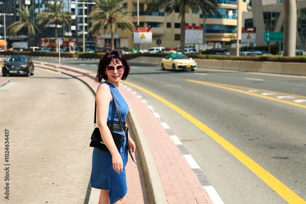 Fototapeta premium A woman in a summer dress walks along a busy road city.